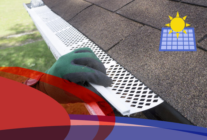 Close-up of a worker wearing gloves installing a white, perforated metal gutter guard screen onto a residential roof gutter
