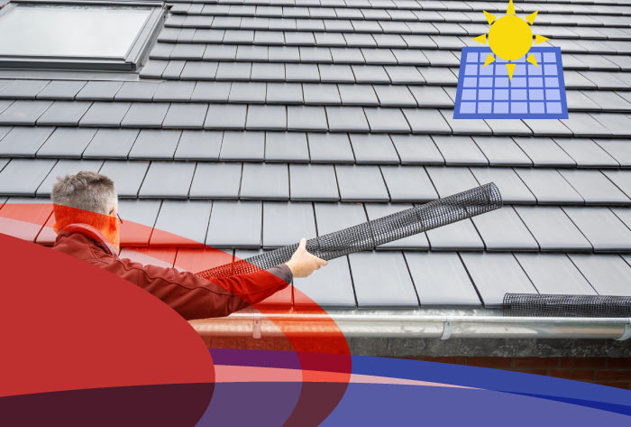 Roofer installing a rolled section of black plastic mesh gutter guard (foam insert style) onto a light-colored tile roof showing how do gutter guards work