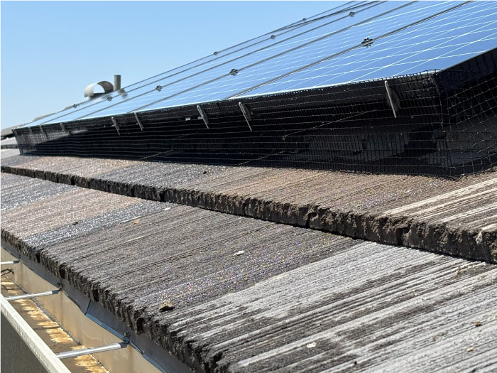 Close-up view of dark wire mesh bird proofing installed underneath a row of residential solar panels to prevent pigeon nesting.