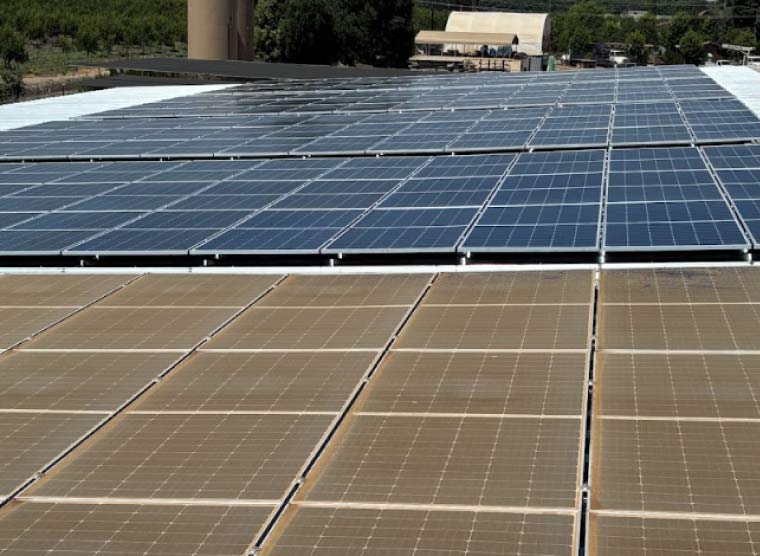 A large commercial rooftop solar array showing a dramatic side-by-side comparison where the bottom half is covered in thick brown Central Valley dust and the top half is professionally cleaned to a deep blue shine.